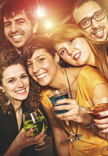 Three young women and two young men close together holding green, blue, and amber drinks and smiling