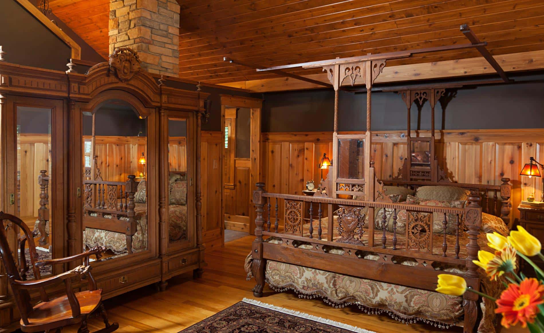 Rustic room with pine ceiling, walls and floor, elaborately carved king sized bed, and mirrored cabinet with triple doors