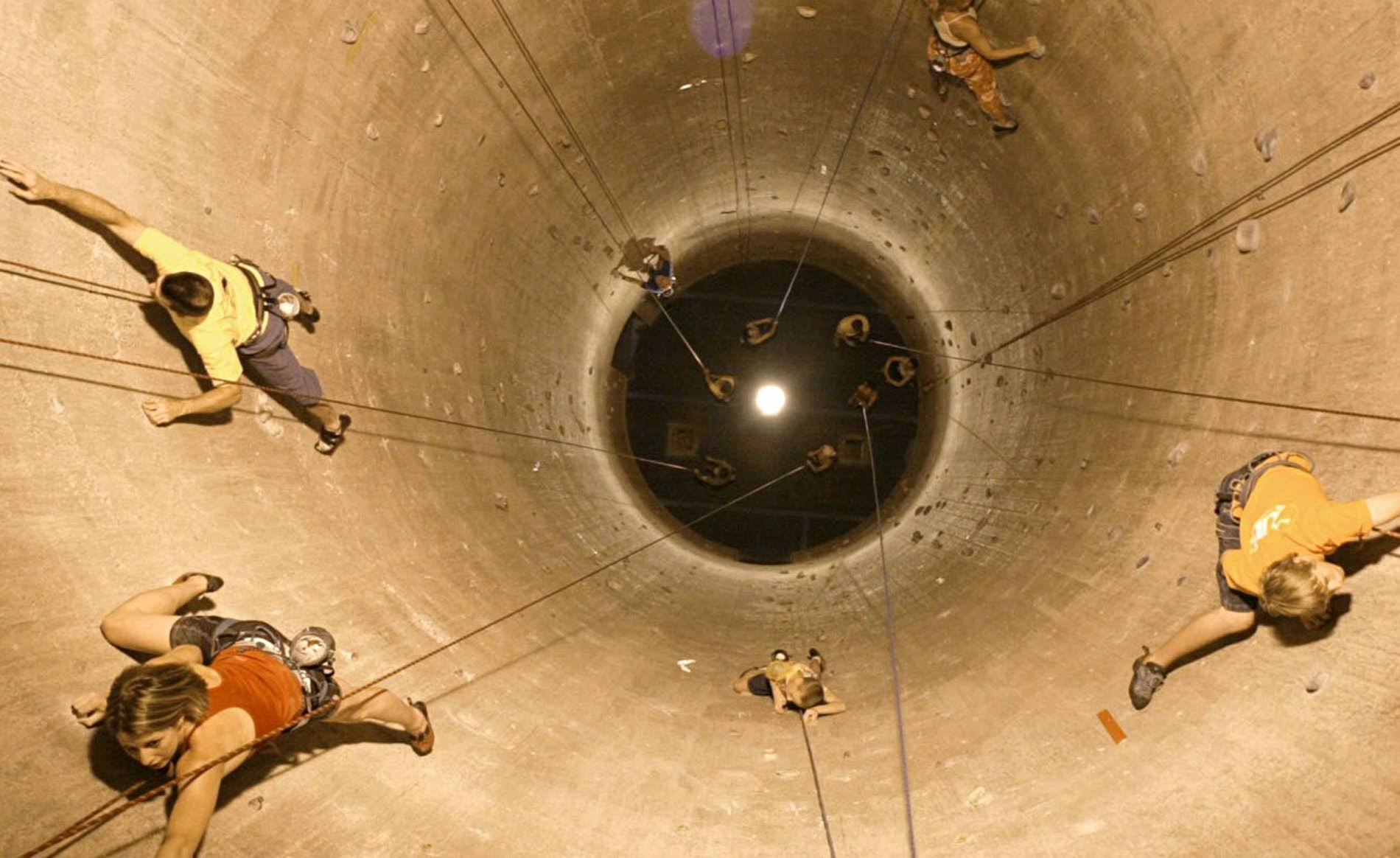 Gray tunnel simulating rock climbing with several people attached to ropes while climbing toward the top
